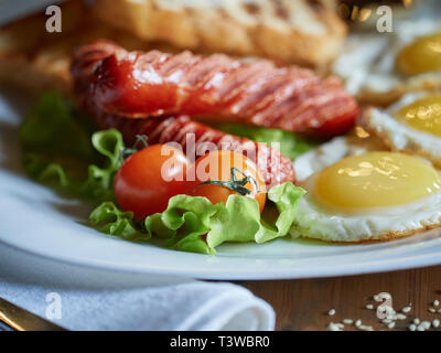 Plusieurs oeufs frits sont servis sur une assiette avec de la saucisse et salade verte avec des tomates rouges frais. Banque D'Images
