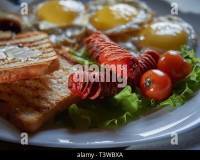 Plusieurs oeufs frits sont servis sur une assiette avec de la saucisse et salade verte avec des tomates rouges frais. Banque D'Images