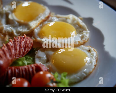 Plusieurs oeufs frits sont servis sur une assiette avec de la saucisse et salade verte avec des tomates rouges frais. Banque D'Images