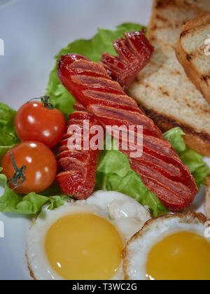 Plusieurs oeufs frits sont servis sur une assiette avec de la saucisse et salade verte avec des tomates rouges frais. Banque D'Images