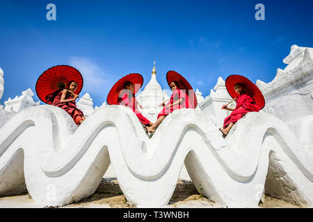 Les moines asiatiques assis sous les parasols au temple historique, Mingun, Mandala, Myanmar Banque D'Images