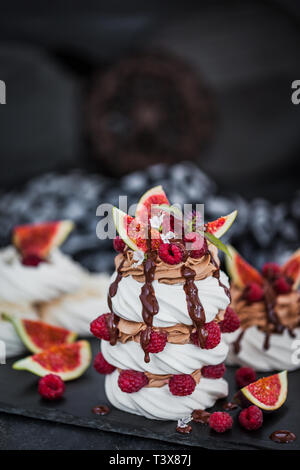 De délicieux gâteaux à la meringue Pavlova décoré de crème au chocolat, figues fraîches et framboises sur fond sombre Banque D'Images
