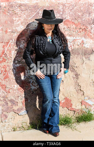 Young Girl wearing cowboy bottes et un chapeau noir s'appuie contre un mur dans une petite ville du sud-ouest de l'Arizona. Banque D'Images