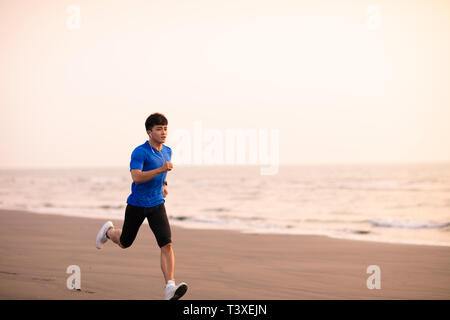 Jeune homme qui court sur la plage au coucher du soleil Banque D'Images