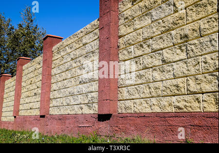 Clôture faite de briques et de plâtre décoratif. Clôture jaune rouge avec éléments. L'escrime de haut et beau. Banque D'Images