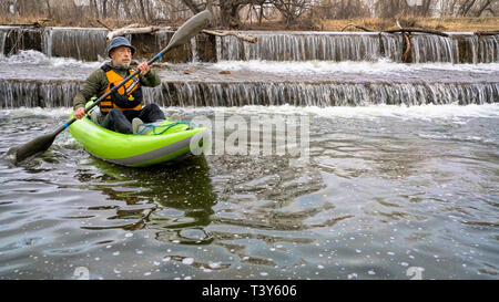 Kayakiste senior est une pagaie whitewater kayak gonflable sur une rivière en dessous d'un barrage de dérivation - Powder River à Fort Collins, Colorado au début du printemps s Banque D'Images