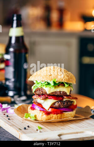 Cheeseburger avec deux galettes de boeuf, fromage cheddar, bacon, laitue Iceberg, des tranches de tomate et d'oignon rouge. Bouteille de bière et des ingrédients sur tabl Banque D'Images