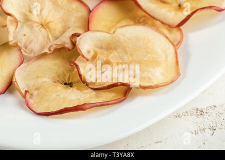 Close-up sur des tranches de pommes séchées naturelles plaque blanche. Chips de fruits, collation santé. Banque D'Images