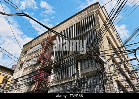 Faible angle de vue d'un ancien bâtiment d'entreprise de grande hauteur et d'un fouillis de câbles et lignes électriques dans le district de Binondo chinois principalement, Manille, Philippines Banque D'Images