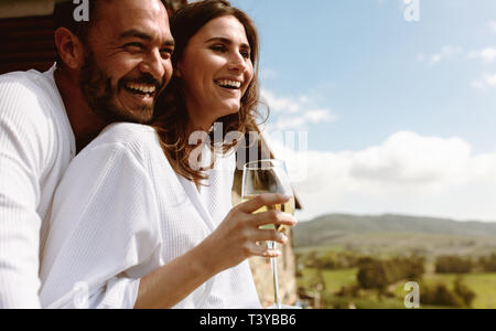 Close up of a smiling couple en vacances ensemble dans le balcon d'une maison de campagne. Smiling woman standing avec un verre de vin blanc wifi Banque D'Images