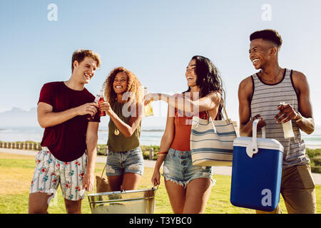 Groupe de personnes transportant des boissons froides et à remous pour partie sur la plage. Groupe varié de jeunes la marche à l'extérieur et avoir des boissons. Banque D'Images