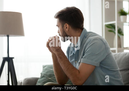 Sérieux attentionné man sitting on sofa at home, perdue dans ses pensées Banque D'Images