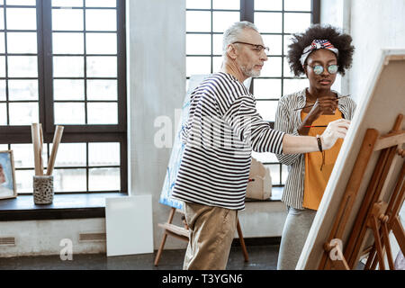 Classe de maître. Célèbre artiste barbu donnant classe de maître pour jeunes talents femme afro-américaine Banque D'Images