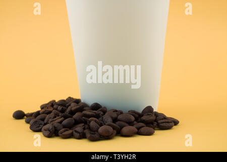 La tasse de café à emporter sur les grains de café, fond jaune. Banque D'Images