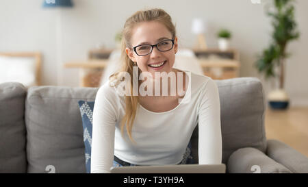 Head shot portrait of smiling woman in glasses, sitting on sofa at home Banque D'Images