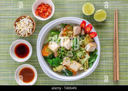 Soupe de nouilles Pho vietnamien végétarien servi dans un bol rond blanc, avec des sauces, de la chaux, piment et fèves germées. Baguettes en bois sur le côté. Vue d'en haut. Banque D'Images