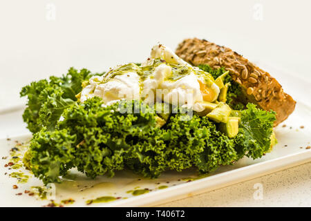 Écraser l'avocat, citron, huile d'olive, deux œufs pochés et fresh kale sur levain, complet avec kale et pesto de basilic. Banque D'Images