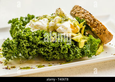 Écraser l'avocat, citron, huile d'olive, deux œufs pochés et fresh kale sur levain, complet avec kale et pesto de basilic. Banque D'Images