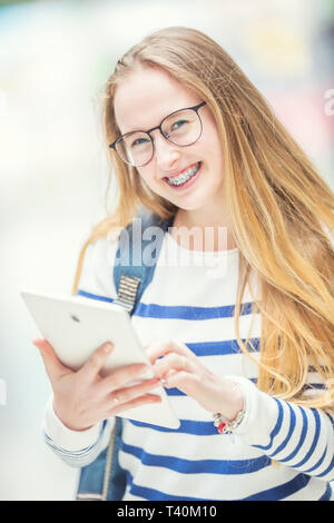 Portrait of a smiling teenage girl avec appareil dentaire. Jeune écolière avec sac d'école et de tablette. Banque D'Images