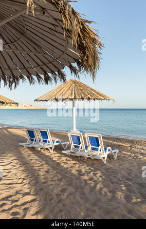 Une chaise longue sous un parapluie. plage de sable avec des palmiers avec une pergola métallique et de chaises longues en plastique. Banque D'Images