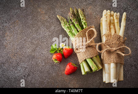 Deux paquets de blanc et vert frais d'asperge couchée sur un fond gris texturé avec copie espace et trois fraises mûres Banque D'Images