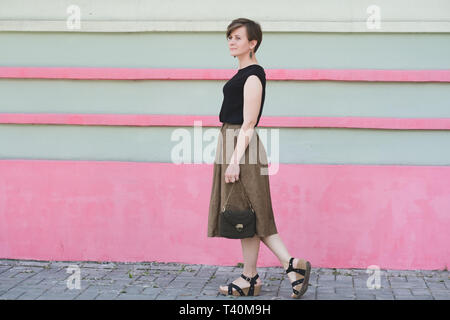 Corps complet de plein air portrait de belle jeune femme à la mode avec petit sac kaki. Cheeful femme marche dans la ville. Banque D'Images