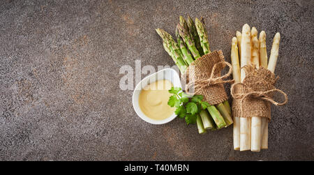 Deux lots de matières premières fraîches asperges vertes et blanches attachées avec une toile sur fond noir en gris texturé avec copie espace en format bannière Banque D'Images