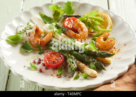 Vert et blanc grillé asperges fraîches avec des crevettes épicées et d'herbes a servi comme apéritif de fruits de mer gastronomique sur une plaque blanche Banque D'Images