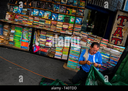 Une libraire salvadorien travaille en face de piles de livres usagés empilés sur la rue dans une librairie d'occasion à San Salvador, El Salvador. Banque D'Images