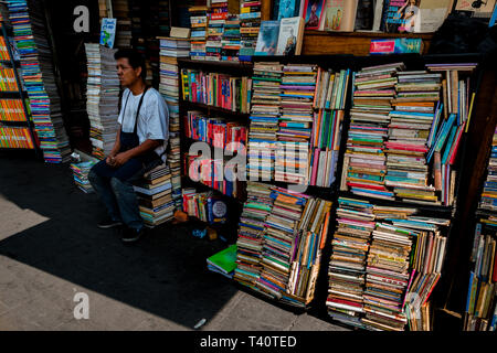 Une libraire salvadorien se trouve devant des piles de livres usagés empilés sur la rue dans une librairie d'occasion à San Salvador, El Salvador. Banque D'Images