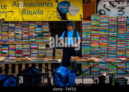 Une libraire salvadorien s'élève face à des piles de livres usagés empilés sur la rue dans une librairie d'occasion à San Salvador, El Salvador. Banque D'Images