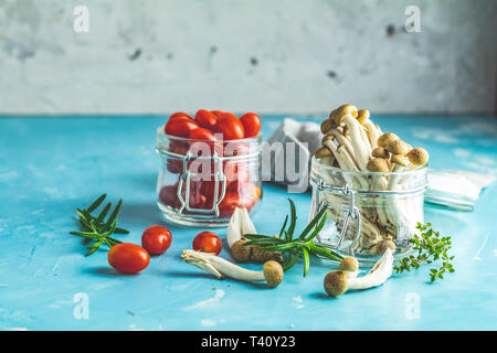 Shimeji Buna - champignon comestible de l'Asie de l'Est. Une bonne alimentation pour une bonne santé. Bouquet de champignons shimeji et tomates cerises en bocaux sur béton bleu surfa Banque D'Images