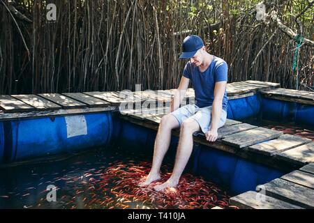 Jeune homme ayant poisson naturel thérapie spa et massage des pieds contre les mangroves dans le lac, au Sri Lanka. Banque D'Images