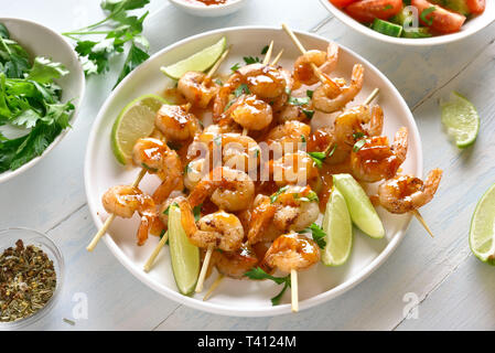 Brochettes de crevettes avec des greens, épices, citron vert et la sauce sur plaque blanche sur table en bois. Brochettes de crevettes grillées. De savoureux fruits de mer. Banque D'Images