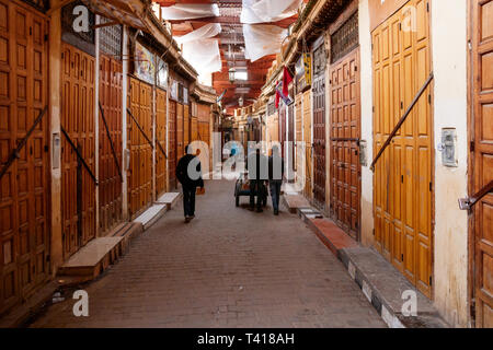 Des personnes non identifiées, balade dans la vieille médina le long des portes fermées des nombreuses boutiques. Fes, Maroc. Banque D'Images