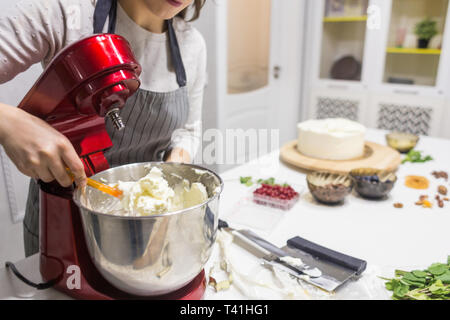 Jeune femme pâtissier bat la crème dans un bol en métal rouge dans un mélangeur électrique. Le concept de pâtisserie maison, la cuisine Banque D'Images