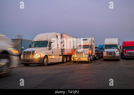 Différents modèles et marques commerciales professionnelles bonnet big rigs camions avec remorques semi semi permanent dans la rangée sur le crépuscule truck stop et illum Banque D'Images