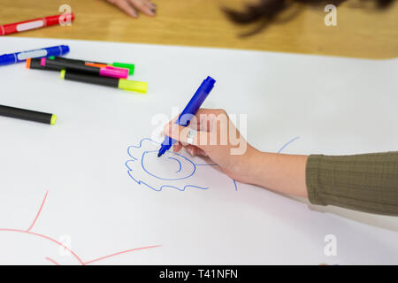 La main d'étudiants avec dessin au feutre bleu sur stickman simple big white paper on desk in classroom. Les stylos colorés renversé sur papier. Concept de l'éducation Banque D'Images