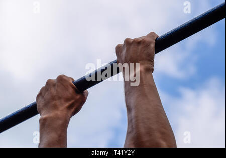 Les mains sur la barre de près. L'homme tire lui-même sur la barre. Faire du sport dans l'air frais. Barre horizontale Banque D'Images