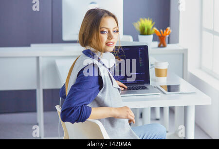 L'accent à l'écoute au casque femme est assis à un bureau avec ordinateur portable, regarde l'écran, prend des notes, apprend la langue étrangère dans internet. Banque D'Images