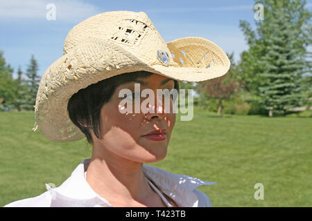 Dark haired woman posing in a park portant un chapeau de paille Banque D'Images
