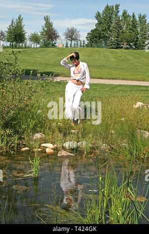 Dark haired woman posing in a park portant un bikini rouge et blanc top blanc, veste et pantalon Banque D'Images