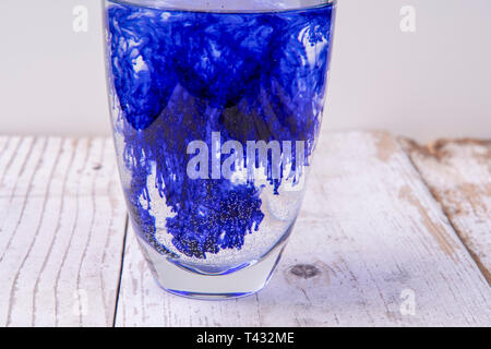 Liquide bleu s'étend dans un verre plein d'eau Banque D'Images