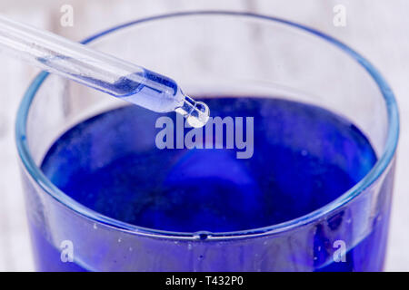 Gouttes de pipette une goutte de liquide dans un récipient de liquide bleu Banque D'Images