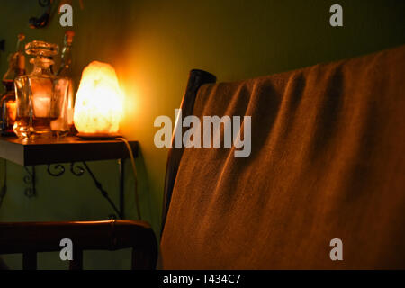 Une photo clé faible d'une scène d'intérieur d'un fauteuil à côté d'une petite table avec une bouteille de whisky éclairé par une lampe de sel de l'Himalaya. Banque D'Images