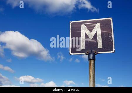 Un panneau routier altérés avec lettre m'indiquer un point de rencontre sur une route étroite contre un bleu ciel nuageux. Banque D'Images