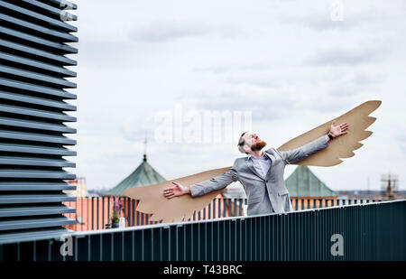 Un jeune homme avec des ailes debout sur une terrasse, battant concept de métaphore. Banque D'Images