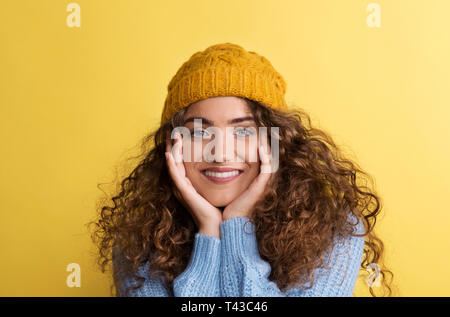 Portrait d'une jeune femme avec bonnet de laine en studio sur un fond jaune. Banque D'Images