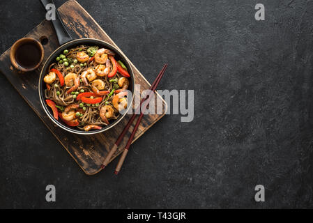 Les sautés avec nouilles soba, crevettes (crevettes) et de légumes. La nourriture saine, de l'Asie repas sautées dans le moule, sur fond noir, vue du dessus. Banque D'Images