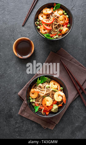 Les sautés avec nouilles soba, crevettes (crevettes) et de légumes. La nourriture saine, de l'Asie sauté de repas au bol sur fond noir, vue du dessus. Banque D'Images
